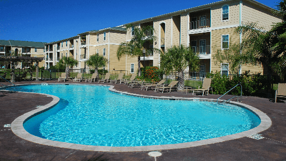 A swimming pool with a multi-family housing complex in the background.