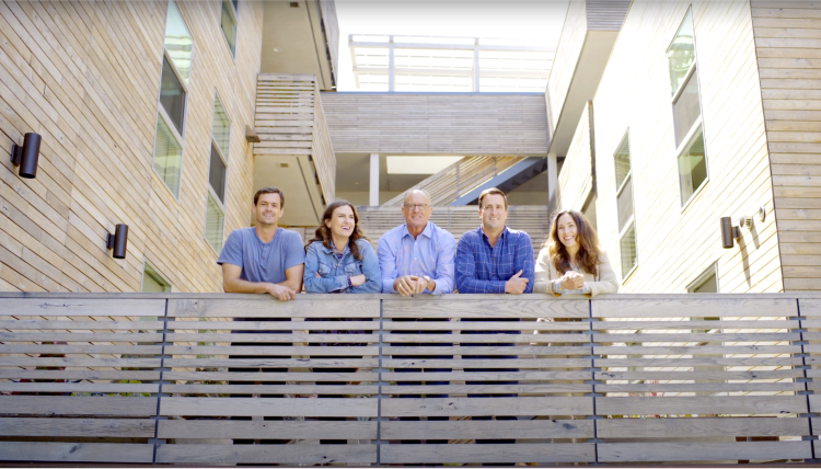 5 people leaning on a wood cladded railing of a multi-family residential courtyard.